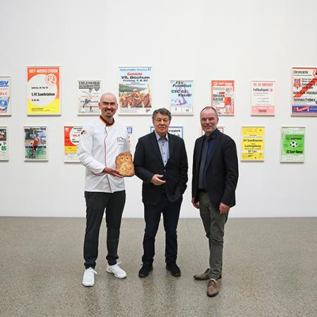 v.l.n.r. Alexander Peter (Bäcker Peter); Otto Rehhagel (Kuratoriumsmitglied der Stiftung Universitätsmedizin und Schirmherr der Aktion Ein Tor – ein Lächeln) und Peter Gorschlüter (Direktor Museum Folkwang) in der Ausstellung Andreas Slominski. Wohnorte gegen Geburtsorte, Foto: Museum Folkwang, Jens Nober, 2024